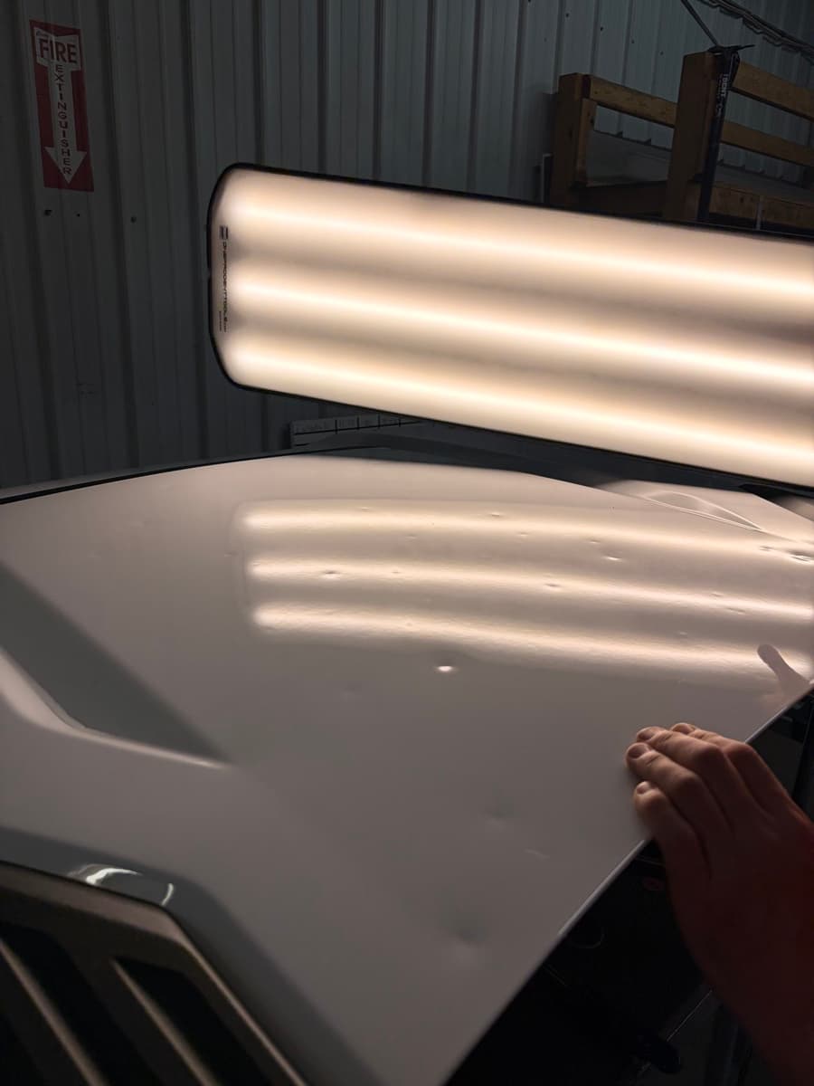 Hail dimples revealed on a white hood under the LED inspection board